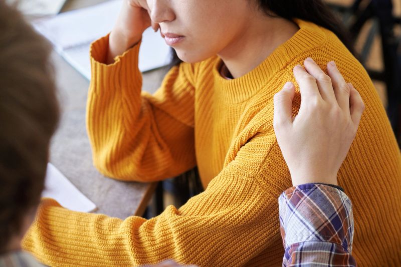 Asian person receiving comforting gesture while sitting at table with paper. Visible emotions of support and connection. Close-up capturing intimate social interaction