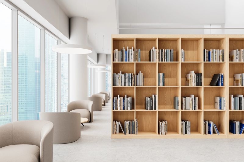 Spacious modern library with wooden bookshelves filled with books, cozy beige armchairs, and large windows overlooking a cityscape, creating a stylish reading space. 3D Rendering