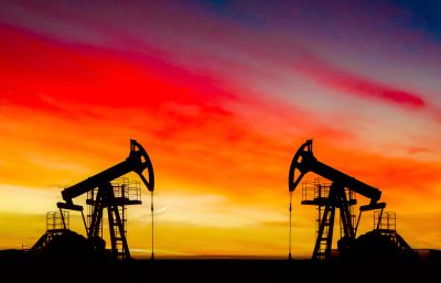 Two oil pump jacks silhouetted against a vibrant sunset sky.