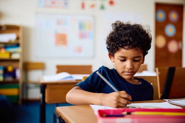 Young boy focused on writing at school desk.