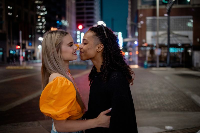 A couple engages in a loving and intimate moment on a vibrant city street. The urban lights enhance the romantic atmosphere, creating a heartwarming scene that highlights affection and connection.