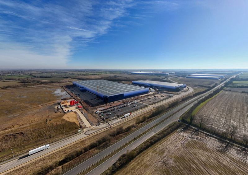 Aerial view of a large distribution center under construction near a highway with trucks driving on a sunny day