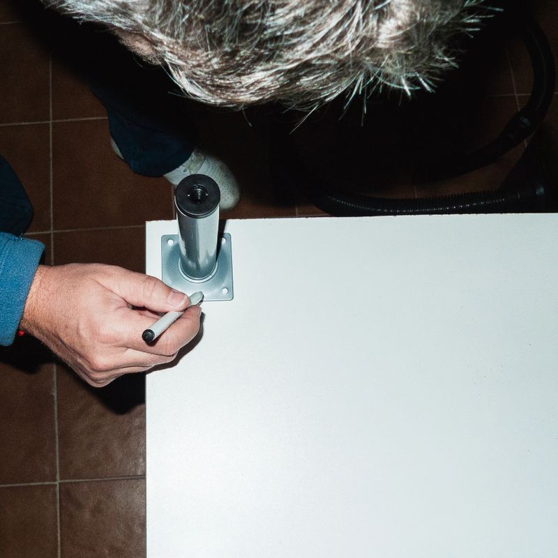 A man is marking with a black marker pen where he is going to put a screw. To do this he is using the small stop that has in its structure the holes where the screws should go. Zenithal image