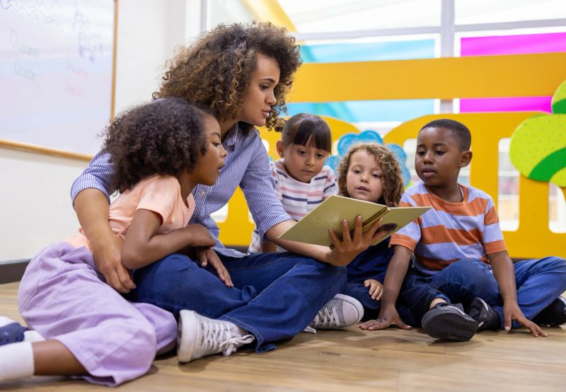 Latin American preschool teacher reading a book to a group of children - education concepts