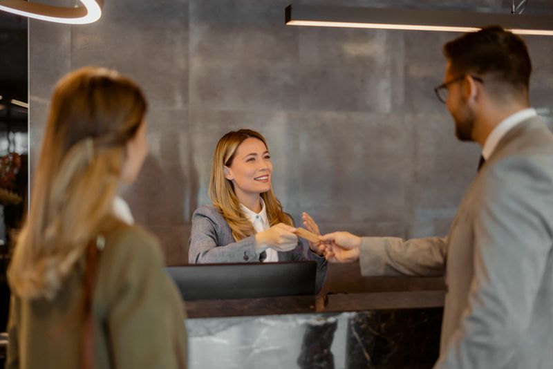 Couple receiving key from hotel room at reception. A professional hotel receptionist assists business travelers with their check-in process at an upscale front desk.