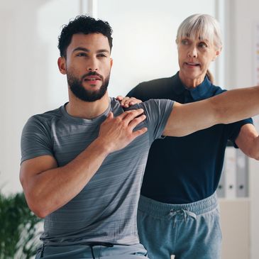 A therapist assists a man with a shoulder stretch during rehabilitation.