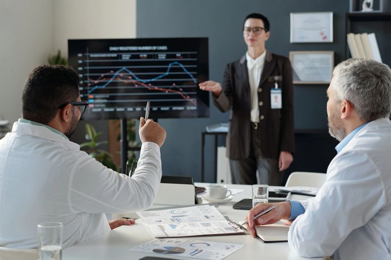 Back view of mature doctor raising hand asking questions during medical conference with speaker in blurred background copy space
