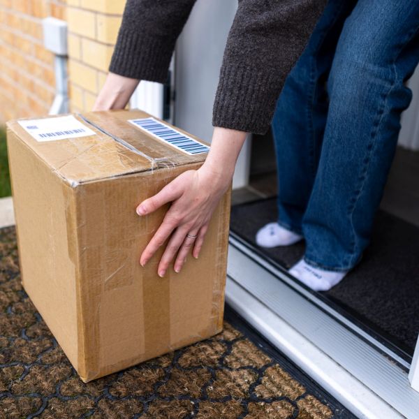 Person picking up a cardboard package at the door.