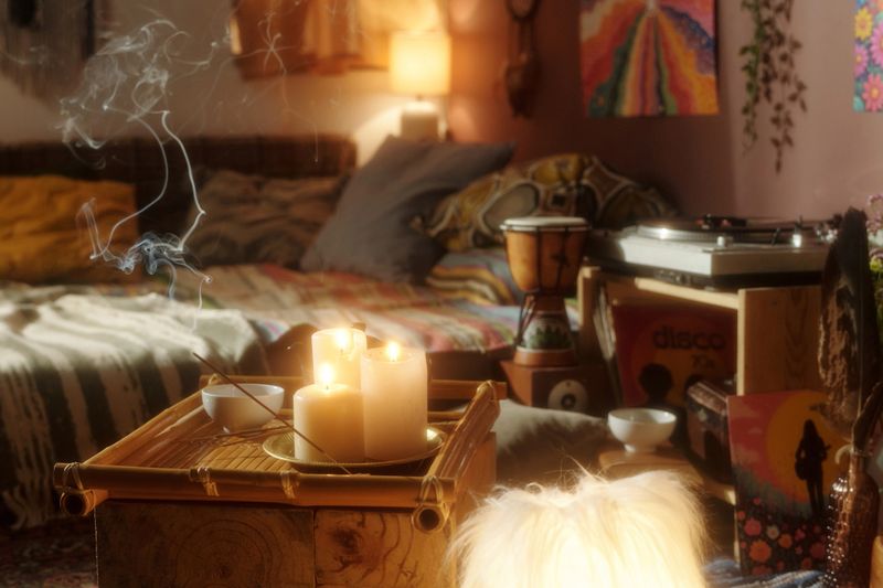 Cozy bohemian room featuring candles, smoke, and various eclectic decor elements. A warm and inviting atmosphere with pillows, posters, and musical instruments enhancing the mood