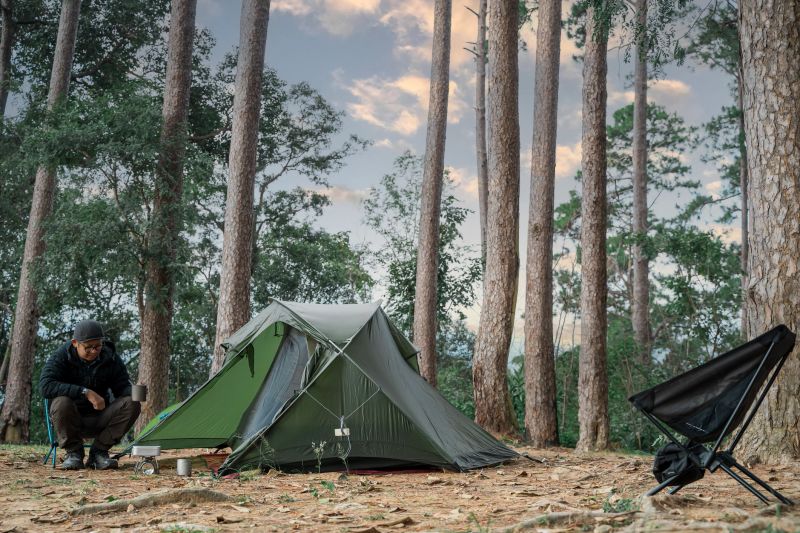 Adventure, hiking and wanderlust concept. Young tourist man holding coffee cup in the tent in morning enjoying the leisure and freedom.