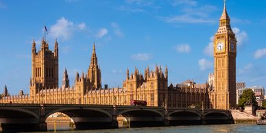 The Palace of Westminster and Big Ben with a red double-decker bus crossing the bridge in London.