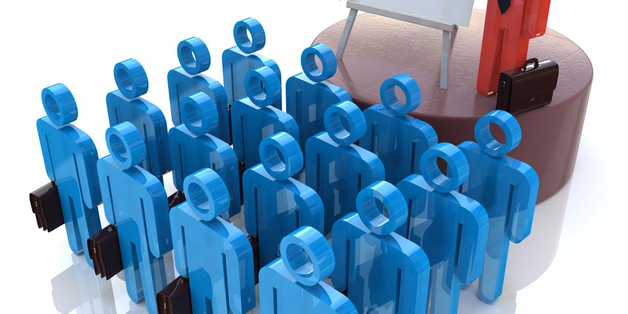 Blue figures listen to a red figure on a stage.