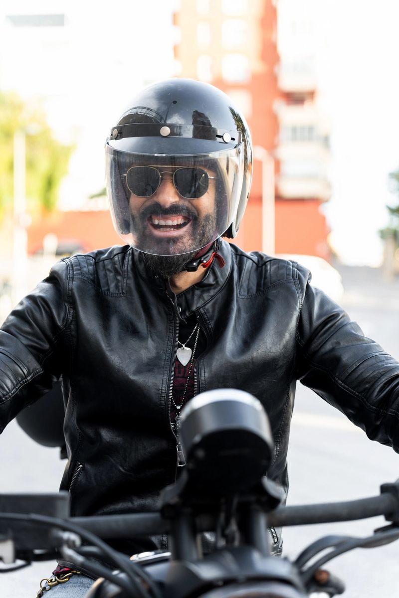 Portrait of a smiling biker wearing a black helmet and leather jacket riding a motorcycle in the city