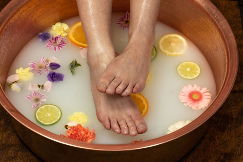 Female feet and ankles soaking in a copper bowl containing a milk bath with flowers