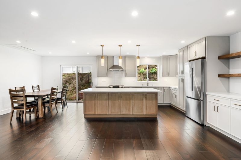 Bright, modern interior featuring a spacious kitchen with a large island, stainless appliances, elegant cabinetry and hardwood flooring.