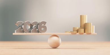 2026 metallic numbers balanced with stacked gold coins on a wooden scale.