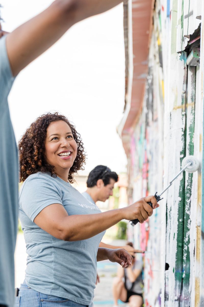 Multiracial group of adults working together, painting a vibrant mural outdoors. Casual clothing, teamwork and community.