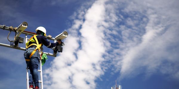 Worker installs security cameras on a pole against a blue sky.