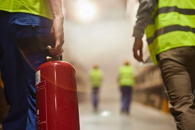 Workers in safety vests with a fire extinguisher in a warehouse.