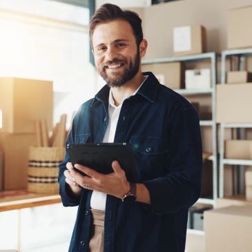 Smiling man holding tablet in a storage room.