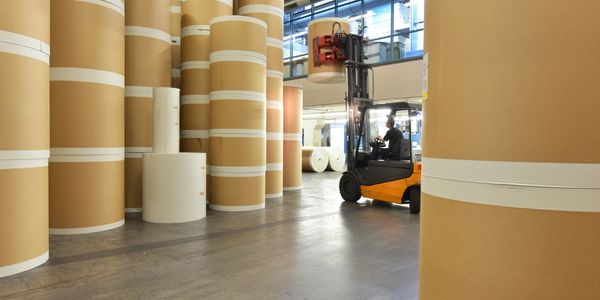 Forklift moving large rolls of paper in a spacious warehouse.