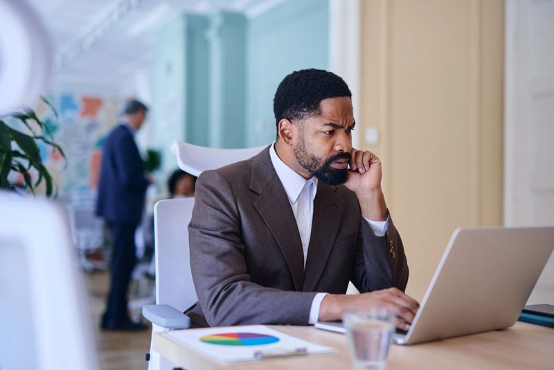 Focused businessman is working on his laptop in a modern office, concentrating on his tasks and analyzing data with a thoughtful expression