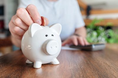 Person putting coin in piggy bank.