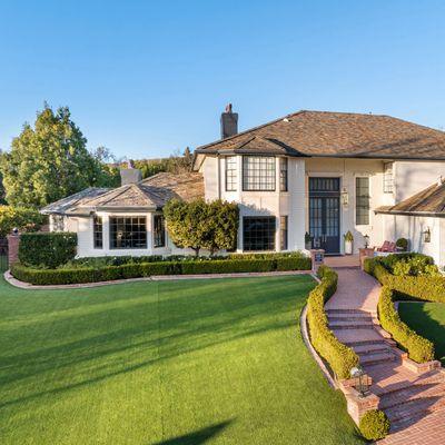 Elegant white house with manicured lawn and curved brick pathway.