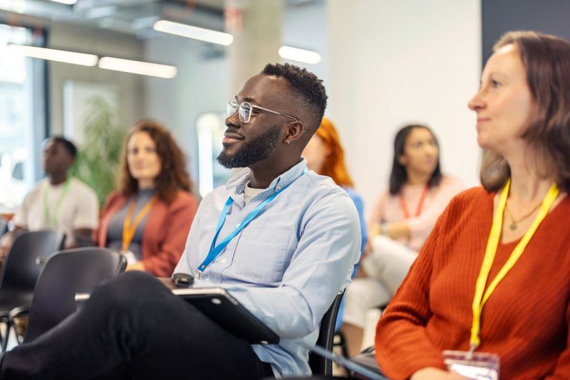 Business professionals from diverse backgrounds attending a seminar at a convention center. Businessman seated in the audience, paying close attention to the conference.