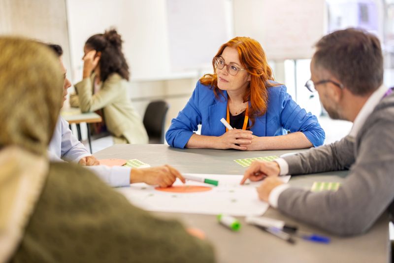 Group of businesspeople seated in small groups at tables actively participating in peer-to-peer learning seminar activities at a convention center. Highlights collaboration, teamwork, and professional development.