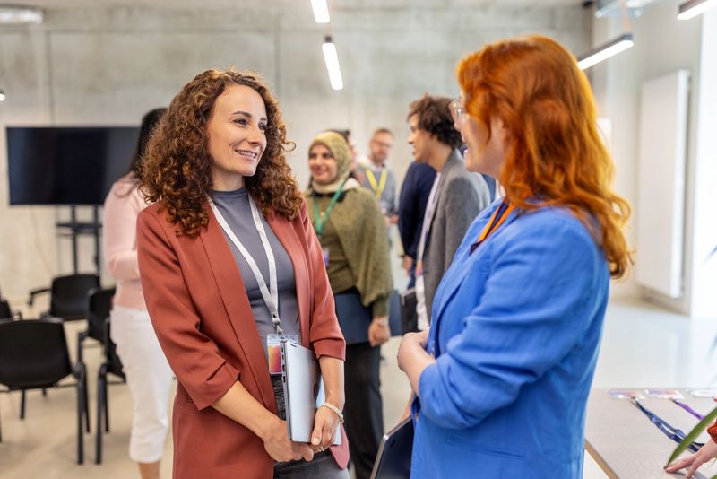 Female professionals attending a networking event, engaging in a conversation before the conference begins at a convention center. Two businesswomen talking during meet and greet session before seminar.