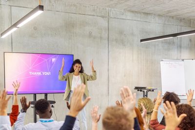 A speaker thanks an engaged audience raising their hands in a modern conference room.