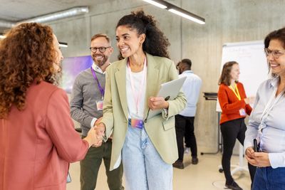 Professional women shaking hands at a networking event in a modern office.