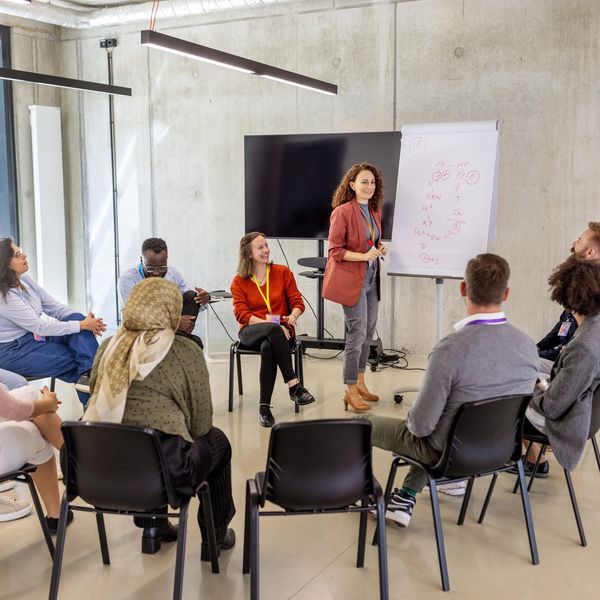 A woman leads a group discussion in a modern meeting room with a flip chart.