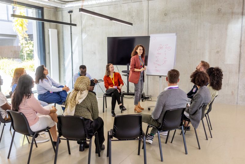 Female professional using a flipchart to explain concepts to a multiracial business audience in a conference hall. Showcases her communication skills and collaborative approach to idea-sharing.