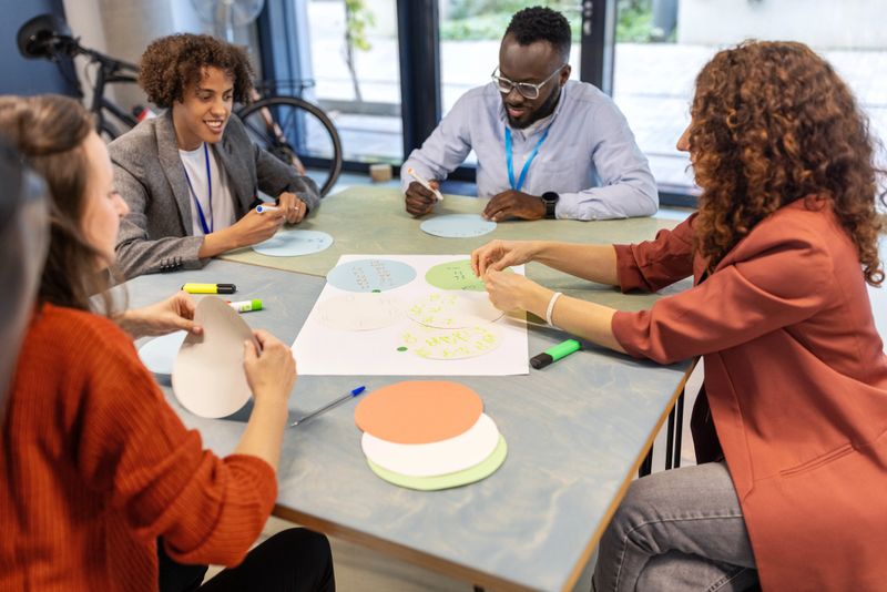 Multiracial group of business professionals seated together at a table and participating in activities during a seminar. Businesspeople participating in seminar activities while seated in small groups at a convention center.