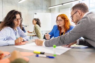 Three adults collaborating on a project with markers and paper in a modern workspace.