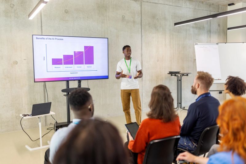 Young businessman delivering a presentation on artificial intelligence with graphical illustrations on a large screen. Showcases his technical expertise and effective communication during a business conference.