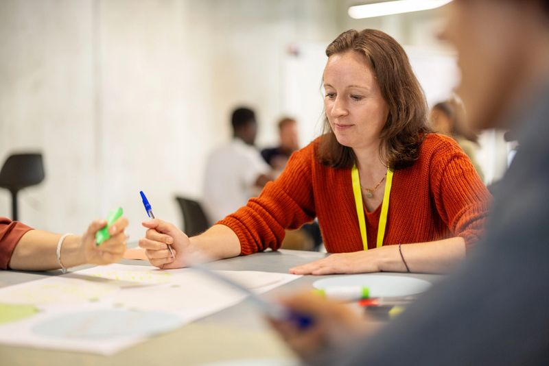 Businesswoman with team members doing seminar activities sitting at a table at a convention center, showcasing her leadership and collaborative approach.