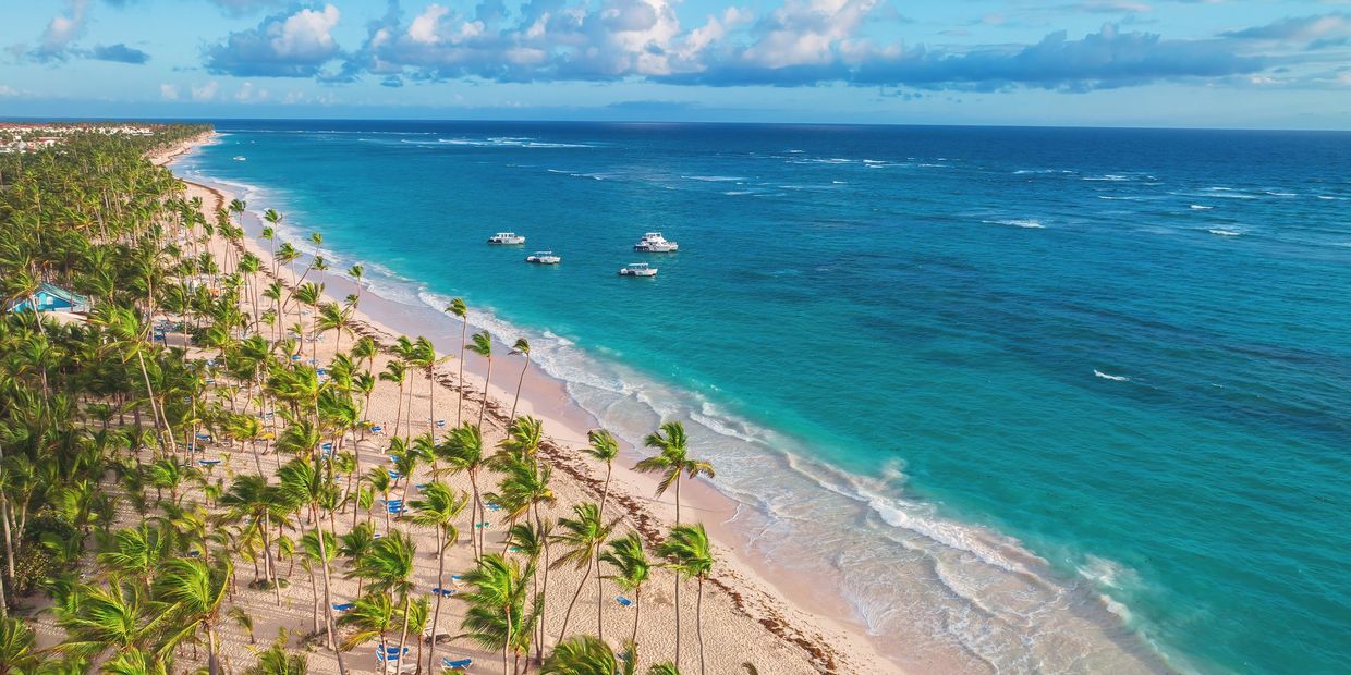 A tropical beach with palm trees and boats on turquoise water.