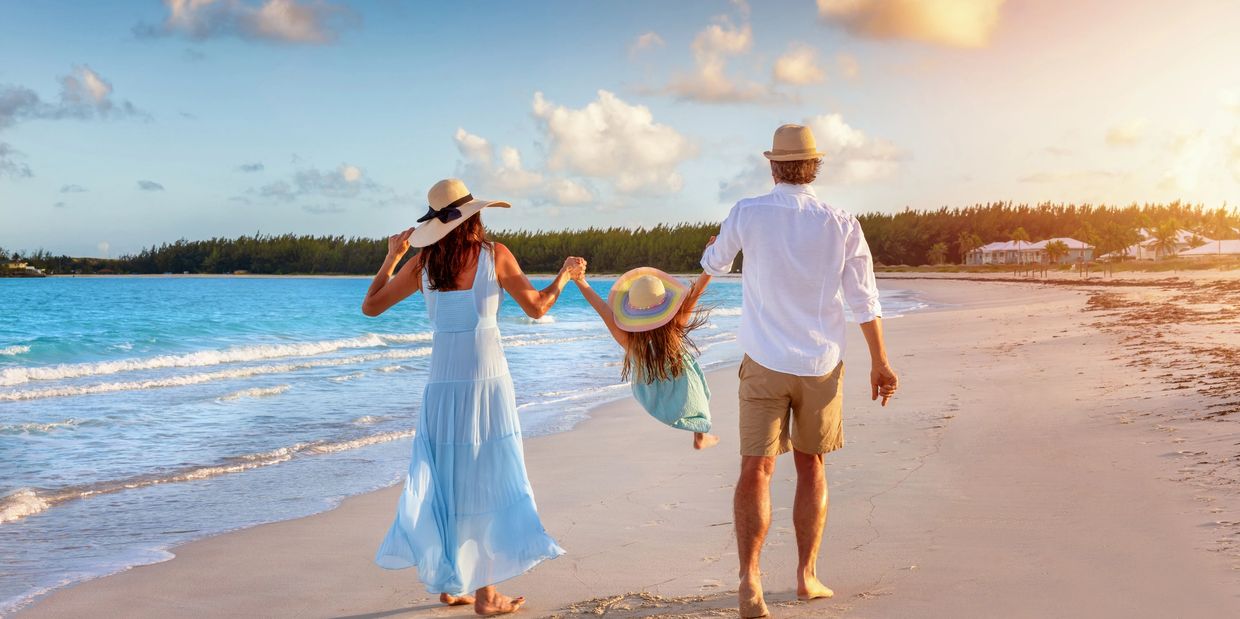 Family enjoying a sunny beach walk, swinging their child between them.