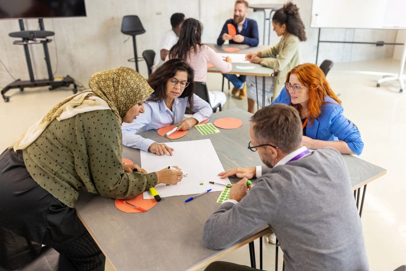 Diverse group of business professionals sitting at tables in small groups and participating in seminar activities. Highlights the spirit of teamwork and interactive learning at a convention center event.