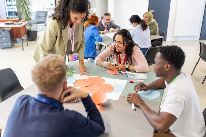 African professional engaging businesspeople at a table, directing group activities during a seminar. Showcases her collaborative approach and effective leadership in a corporate event at a convention center.