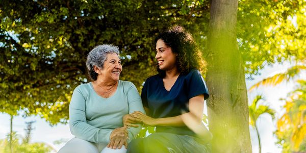 Caregiver supporting elderly man outdoors.