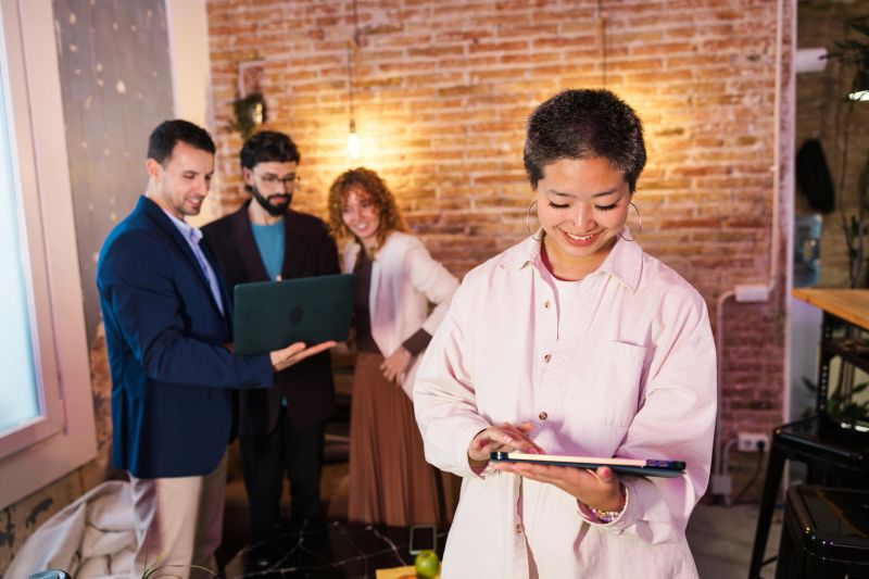 Young asia businesswoman using digital tablet with her colleagues discussing work in background at the office