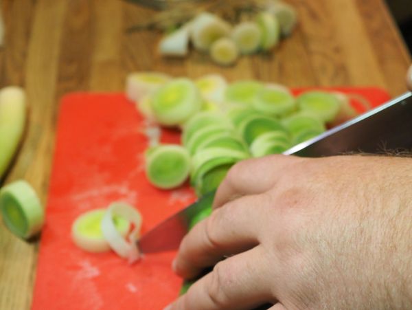 Hand slicing leeks on a red cutting board.
