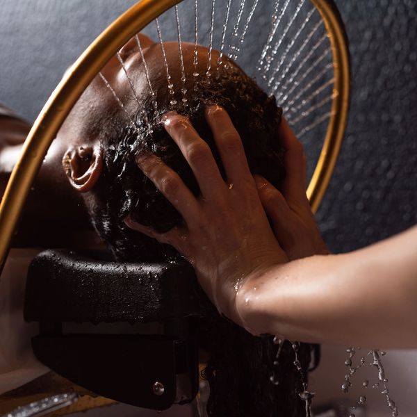 Person washing hair under a circular showerhead with water droplets.