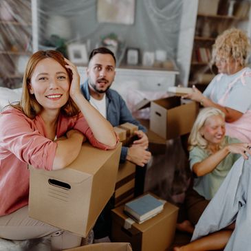 Four friends packing boxes and unpacking clothes in a cozy living room.