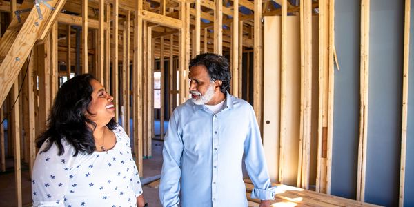 A couple smiles inside a house under construction.