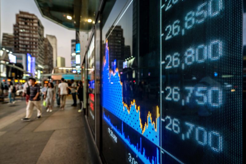 A large outdoor digital display shows stock market trends while people walk by in an urban setting.